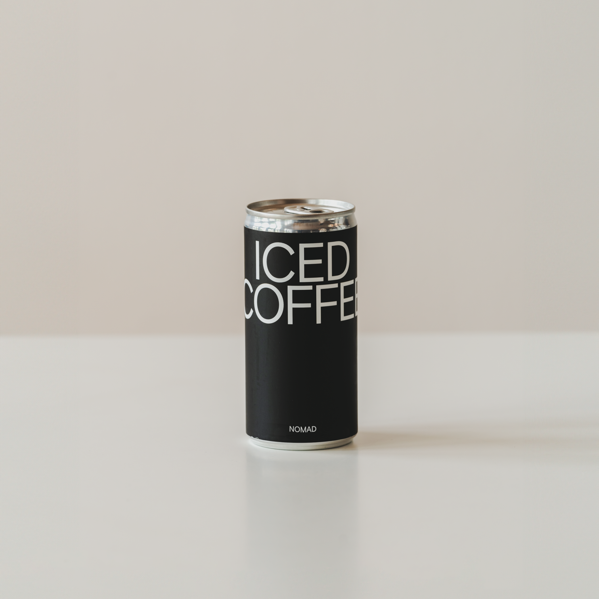 Llauna negra d'Iced Coffee de Nomad amb disseny minimalista i lletres blanques, sobre superfície blanca i fons neutre.