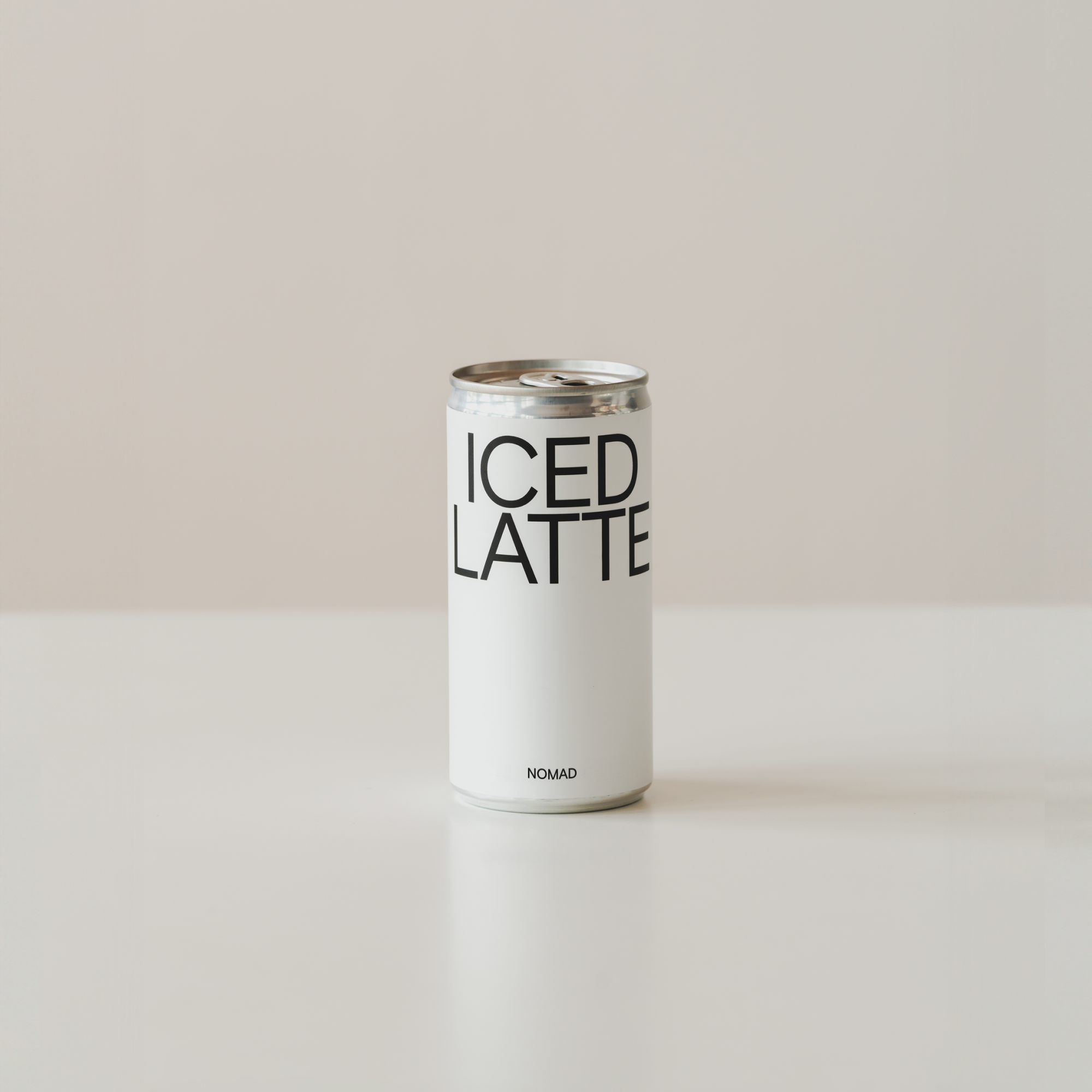 Llauna blanca d'Iced Latte de Nomad amb disseny minimalista en tipografia negra, col·locada sobre una superfície blanca amb fons neutre.